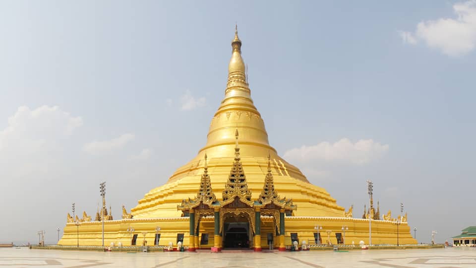 A large golden stupa with intricate designs and a smaller building to its right.