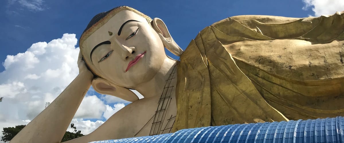 A large Buddha statue with a blue roof, set against a clear blue sky with scattered clouds.