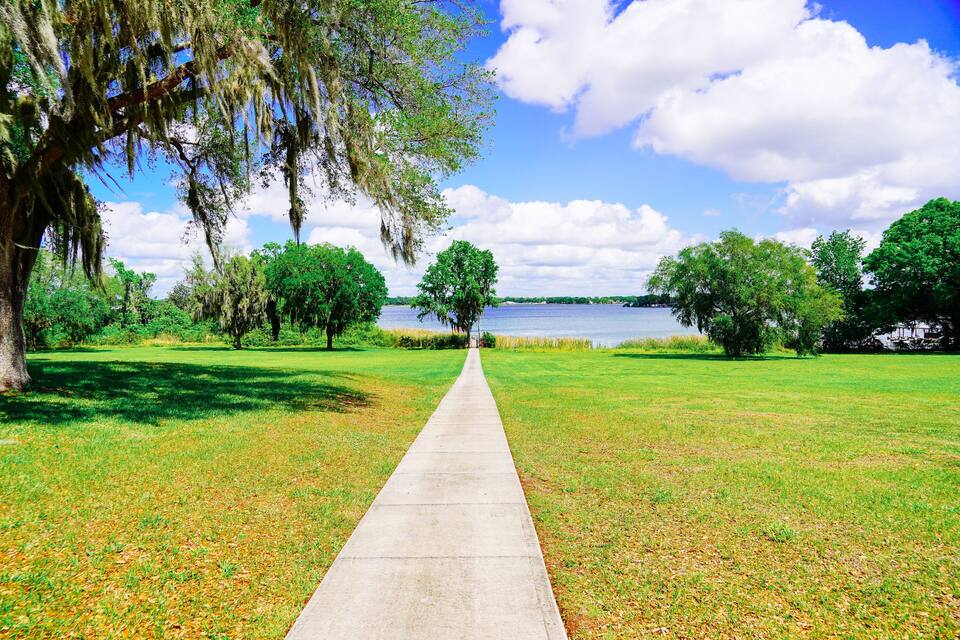 Un chemin en béton qui mène à un lac, avec des arbres et de l’herbe de chaque côté.