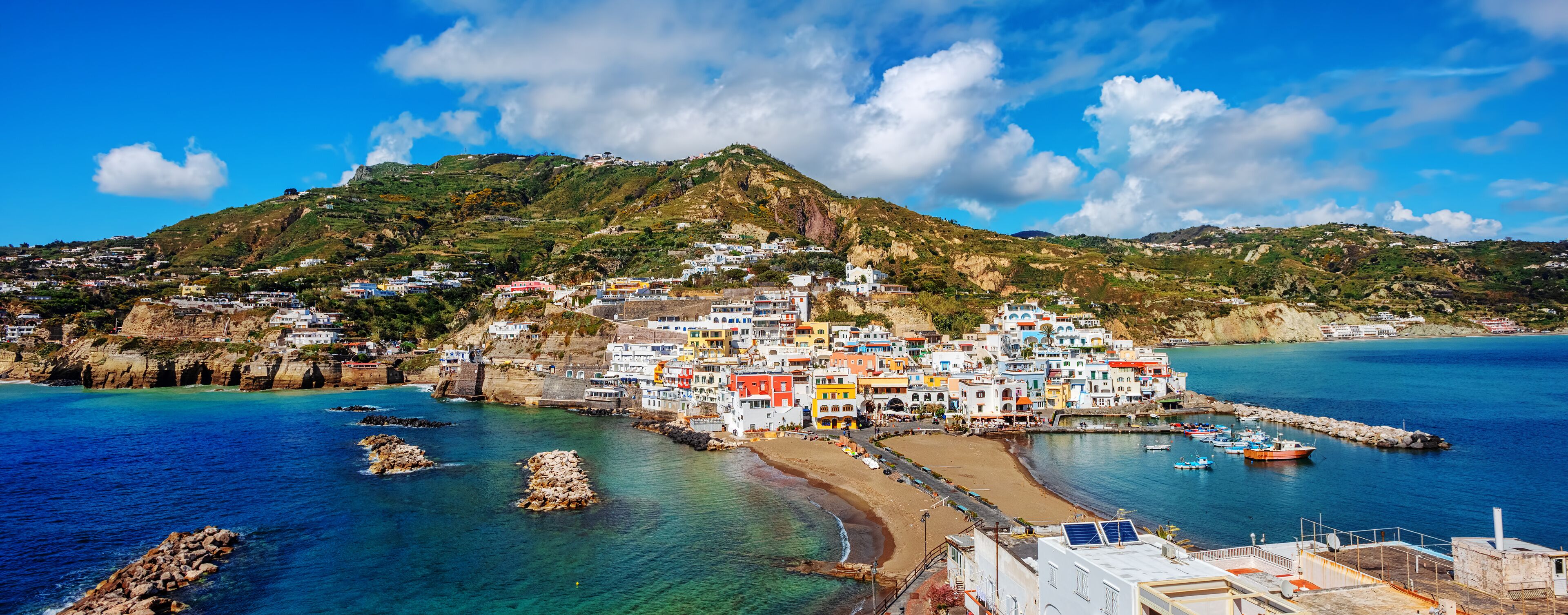 A coastal town with colorful buildings, a beach, and rocky outcrops.