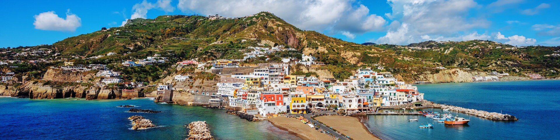 Un pueblo costero con edificios coloridos, una playa y formaciones rocosas.