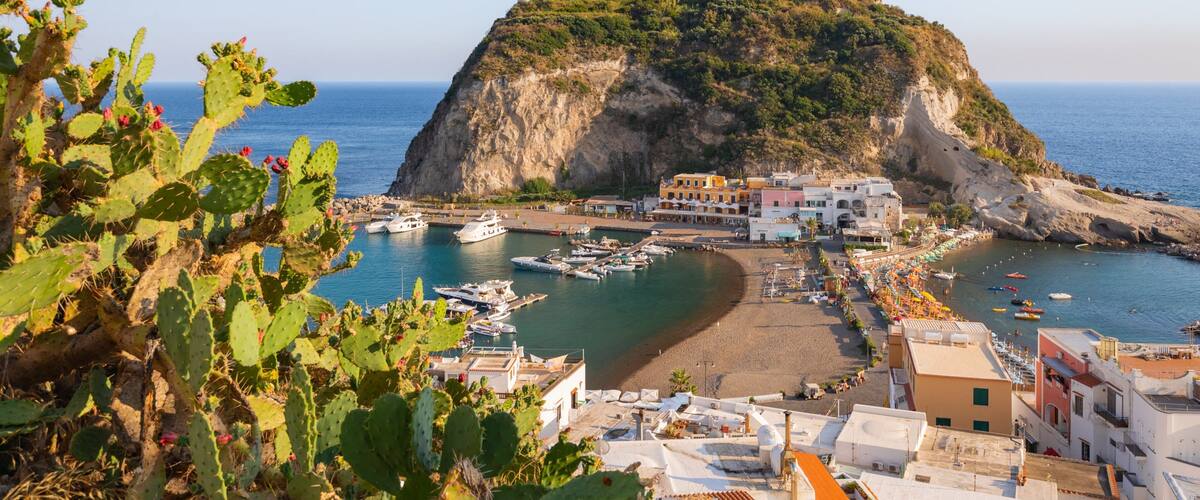 A coastal town with a prominent hill, boats docked at the harbor, and buildings along the waterfront.