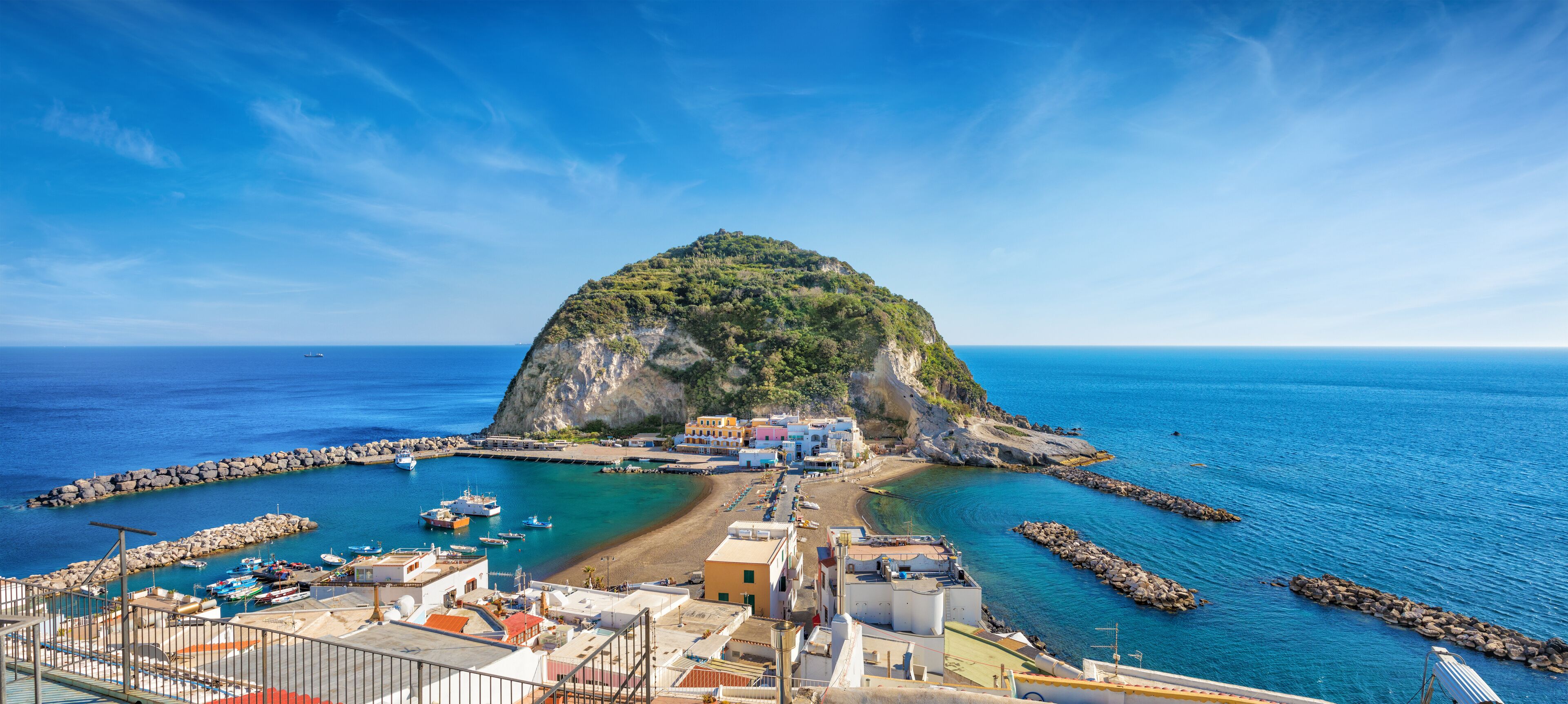 A coastal town with a prominent hill, a marina with boats, and a clear blue sky.