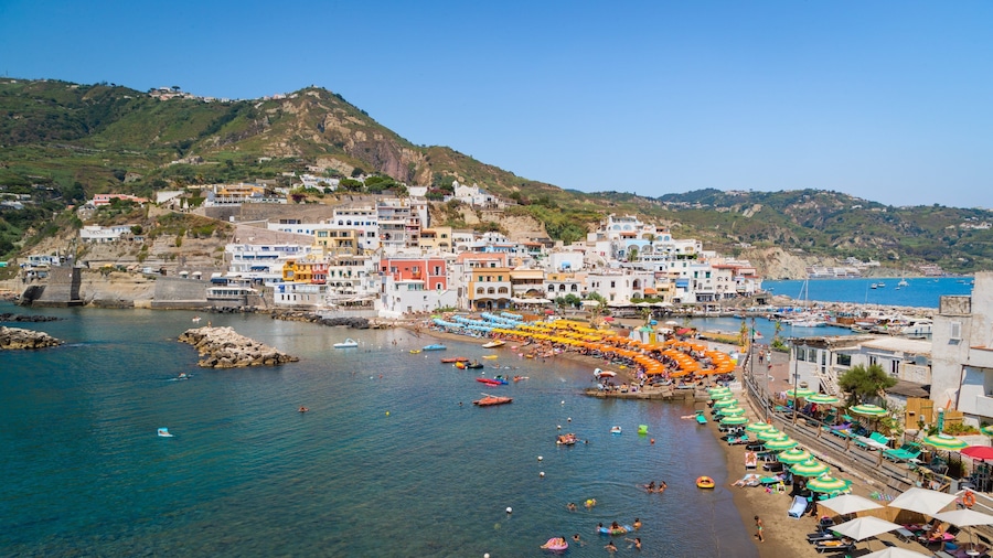 Un pueblo costero con edificios coloridos, una playa con sombrillas y barcos en el agua.