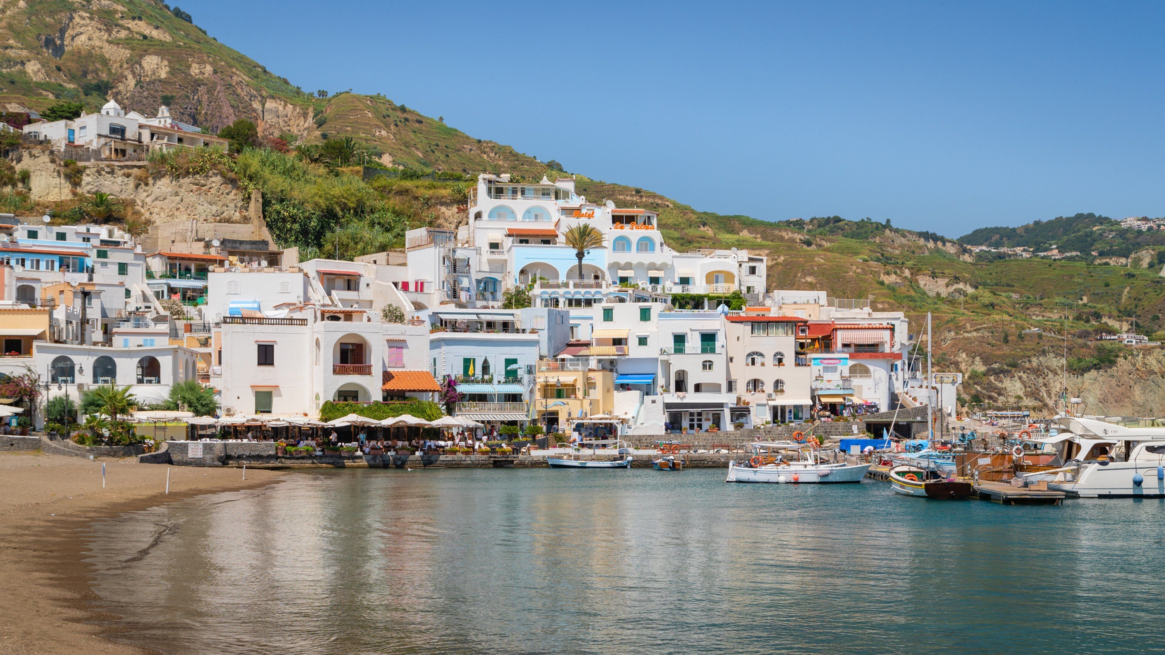 A coastal town with colorful buildings, a beach, and boats docked at the harbor.
