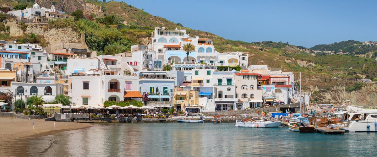 A coastal town with colorful buildings, a beach, and boats docked at the harbor.