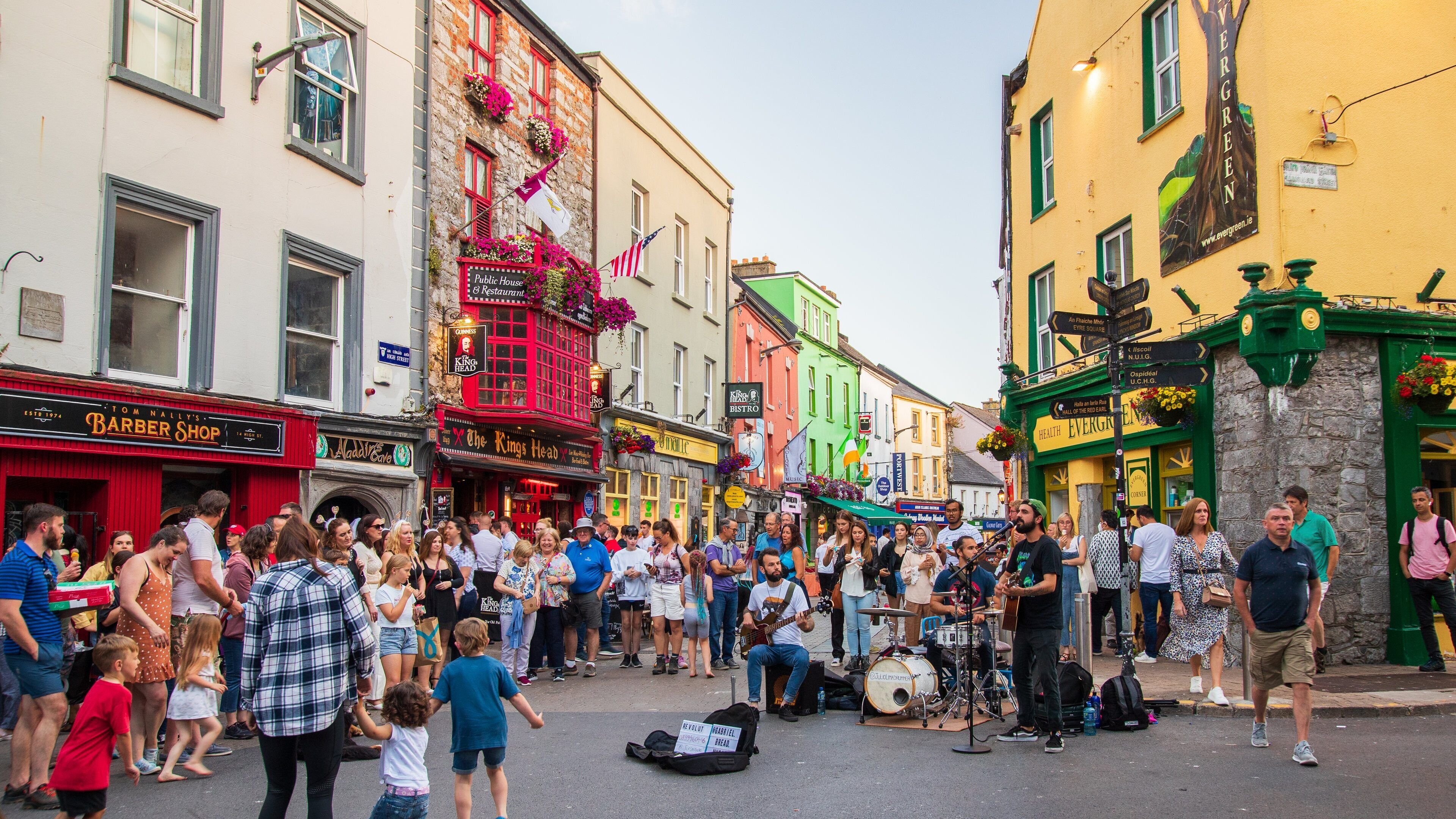 A crowded street with colorful buildings, a public house, and a band performing.