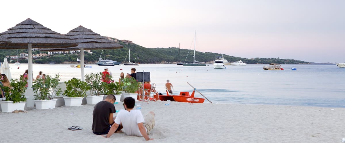 A beach with umbrellas, people, and boats.