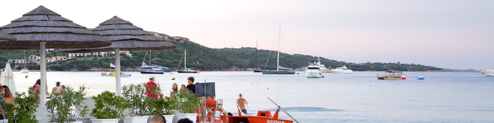 A beach with umbrellas, people, and boats.