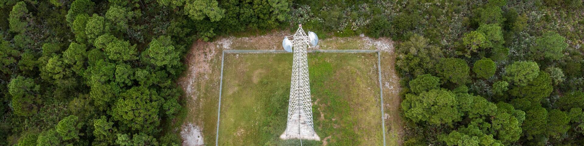 Aerial view of a communications tower surrounded by lush greenery and forest, west of Vero Lakes Estates, Fellsmere, Florida.