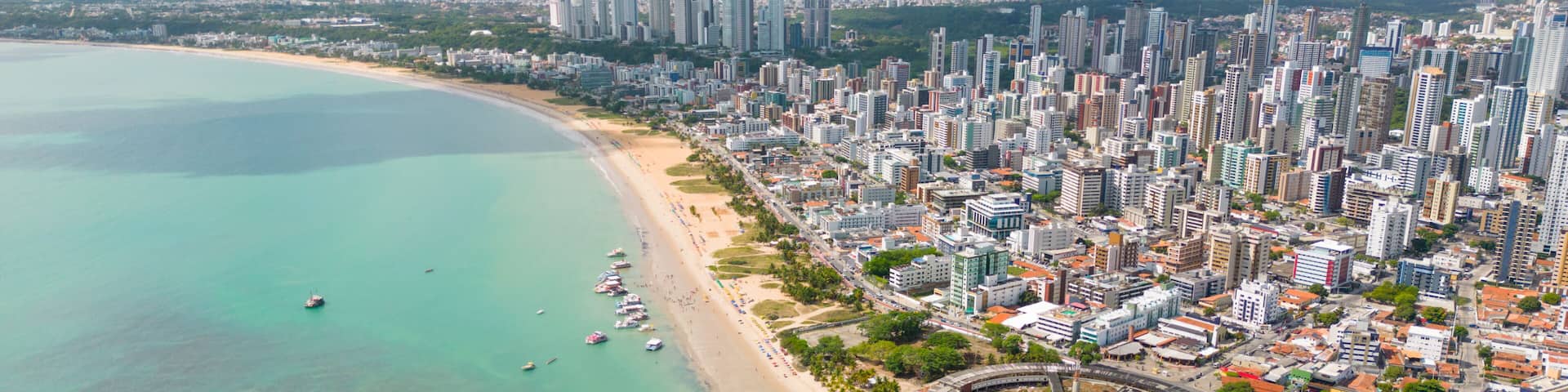 A coastal cityscape with a beach, marina, and dense urban area.