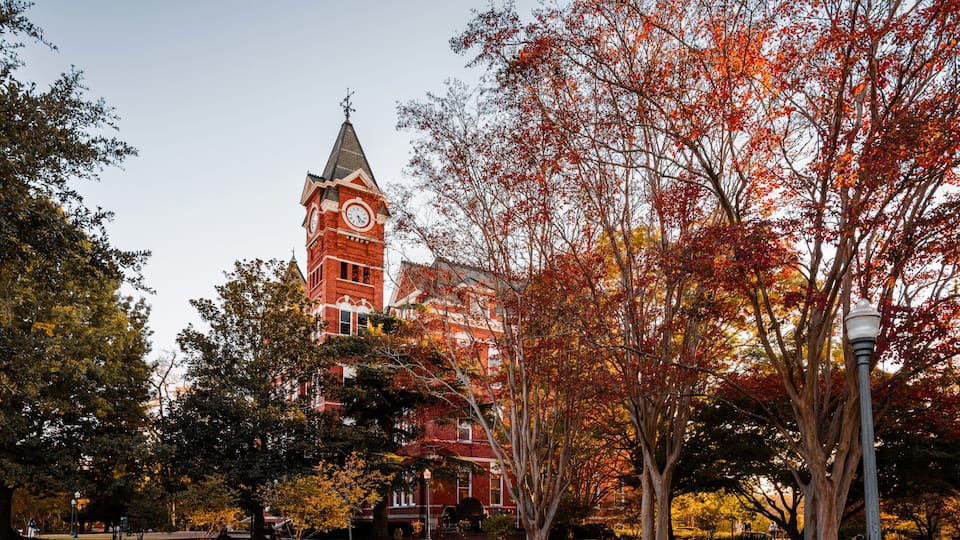 A red brick building with a clock tower, surrounded by trees with autumn leaves.