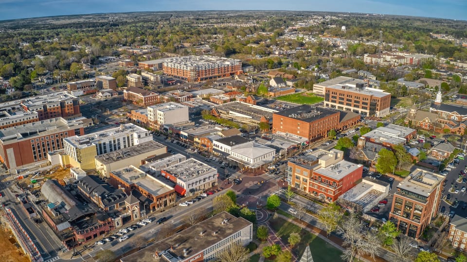 An aerial view of a city with a mix of modern and historic buildings, a river, and surrounding greenery.