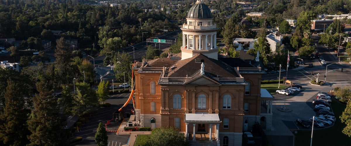 A large brick building with a dome and a tower, surrounded by trees and a parking lot.