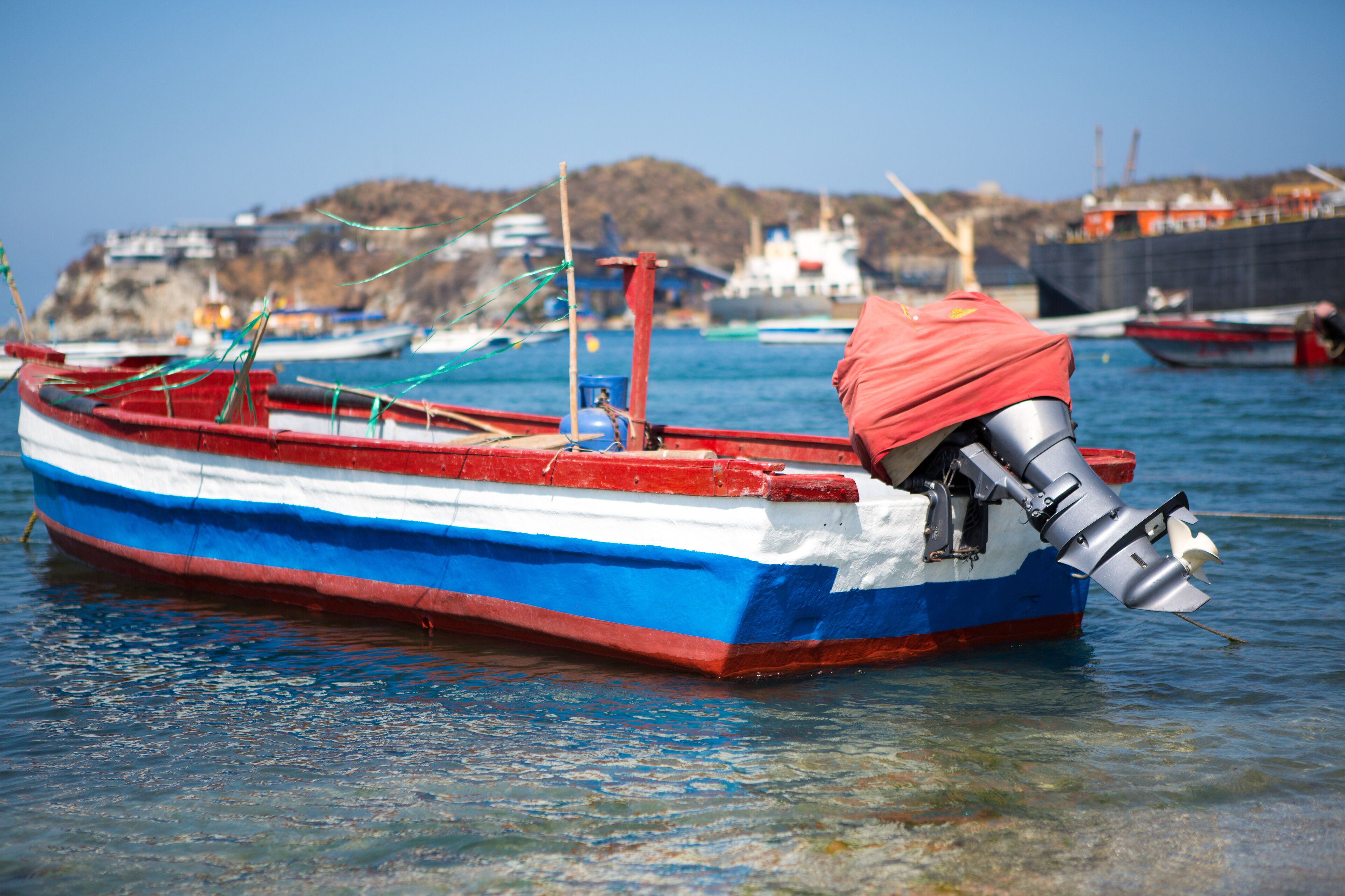 A small boat with a red and blue hull docked at a harbor.