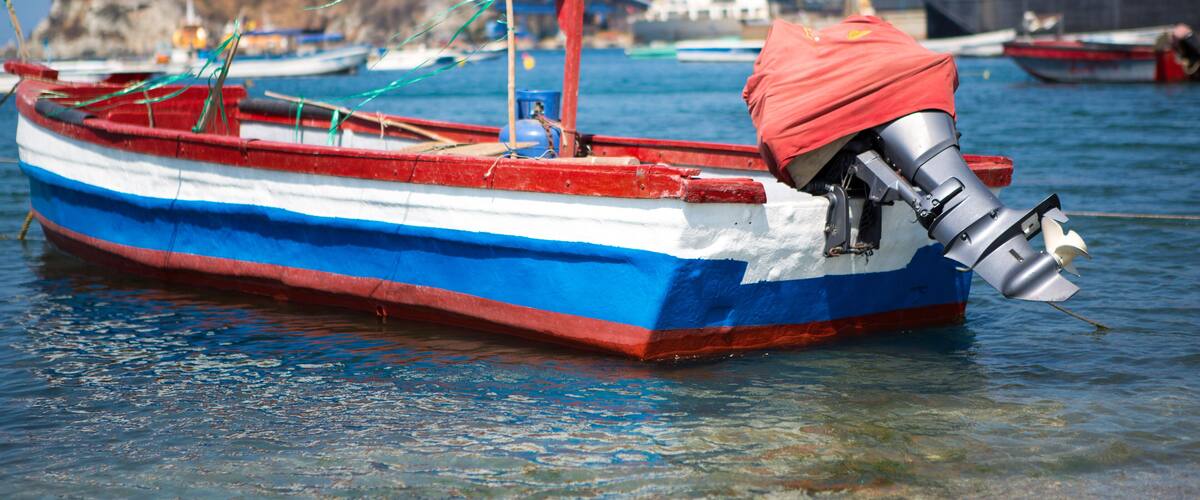 A small boat with a red and blue hull docked at a harbor.