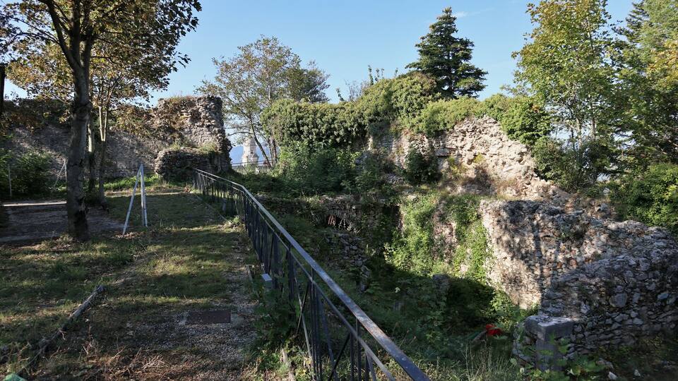 A stone ruin with a metal fence in a wooded area.