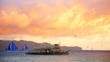 A boat with a blue sail and a wooden structure on the water, with a mountainous landscape in the background.