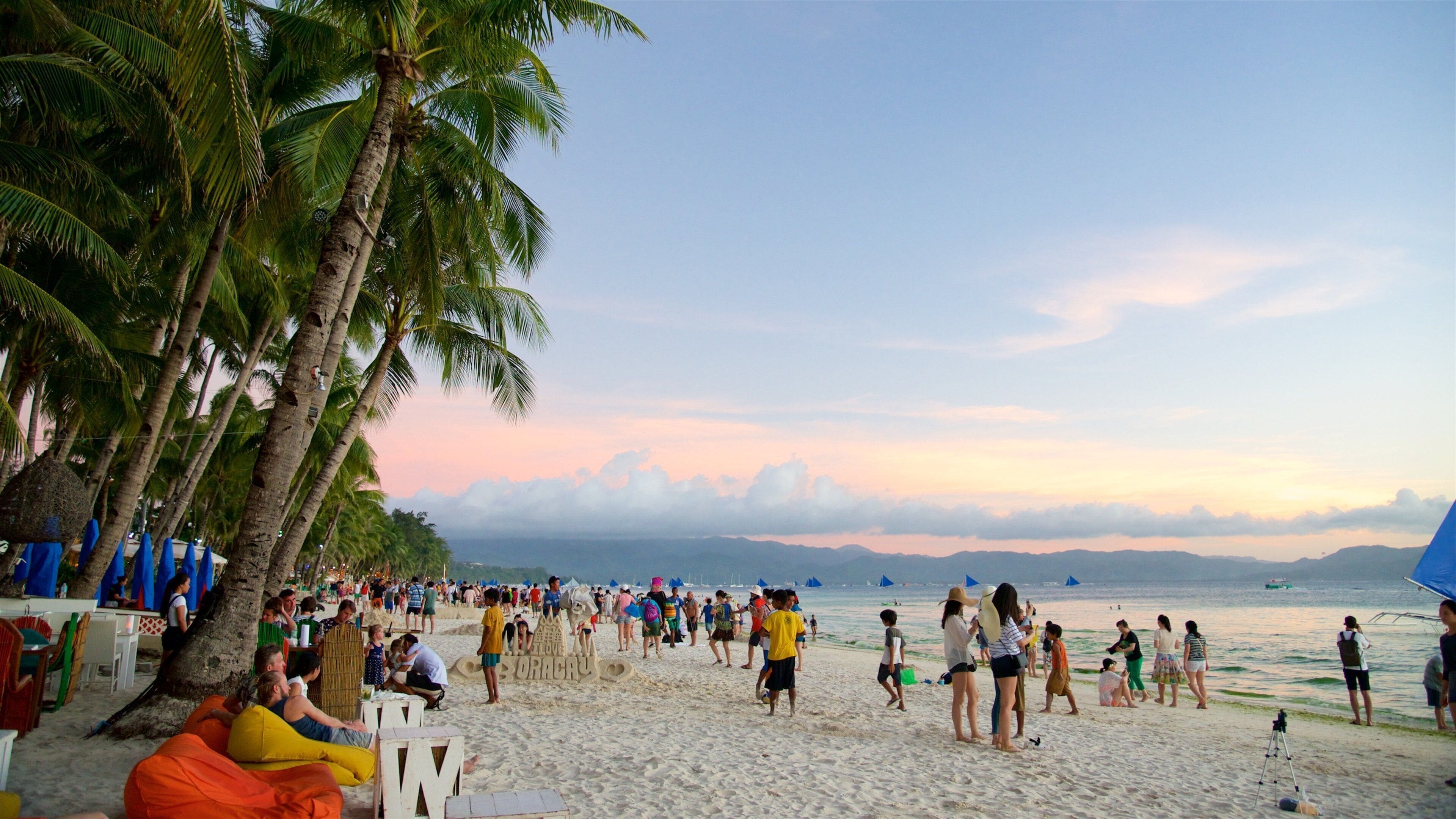 A crowded beach with palm trees and people enjoying the sand.