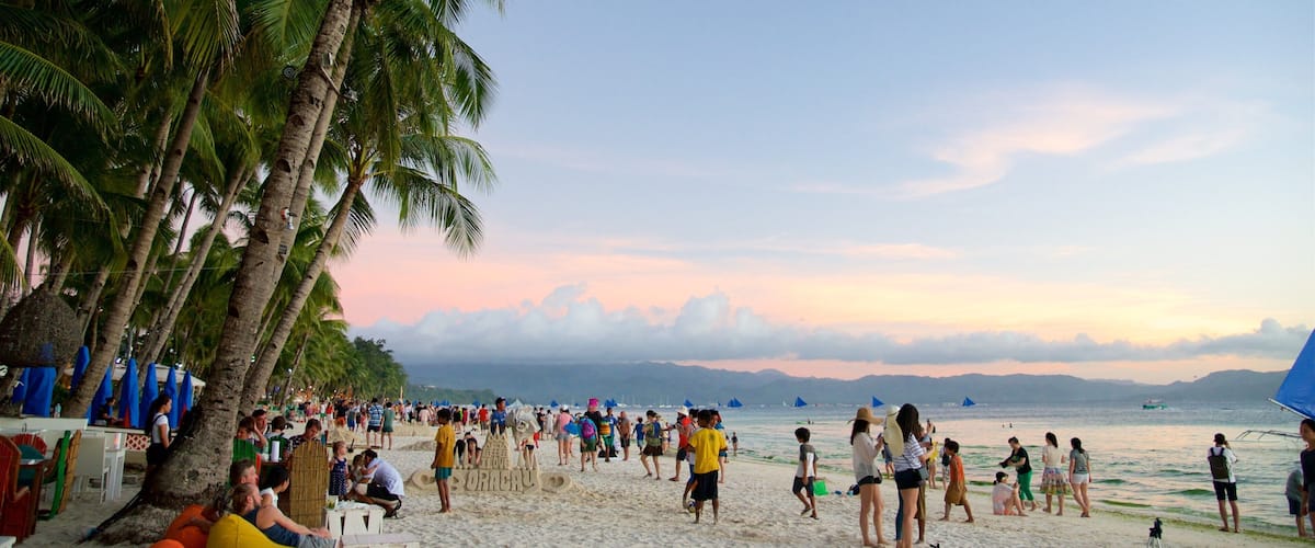 Une plage bondée, avec des palmiers et des gens qui profitent du sable.