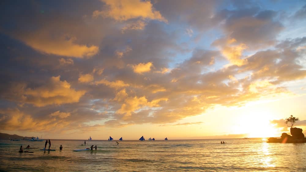 A sunset over the ocean with sailboats and people on surfboards.