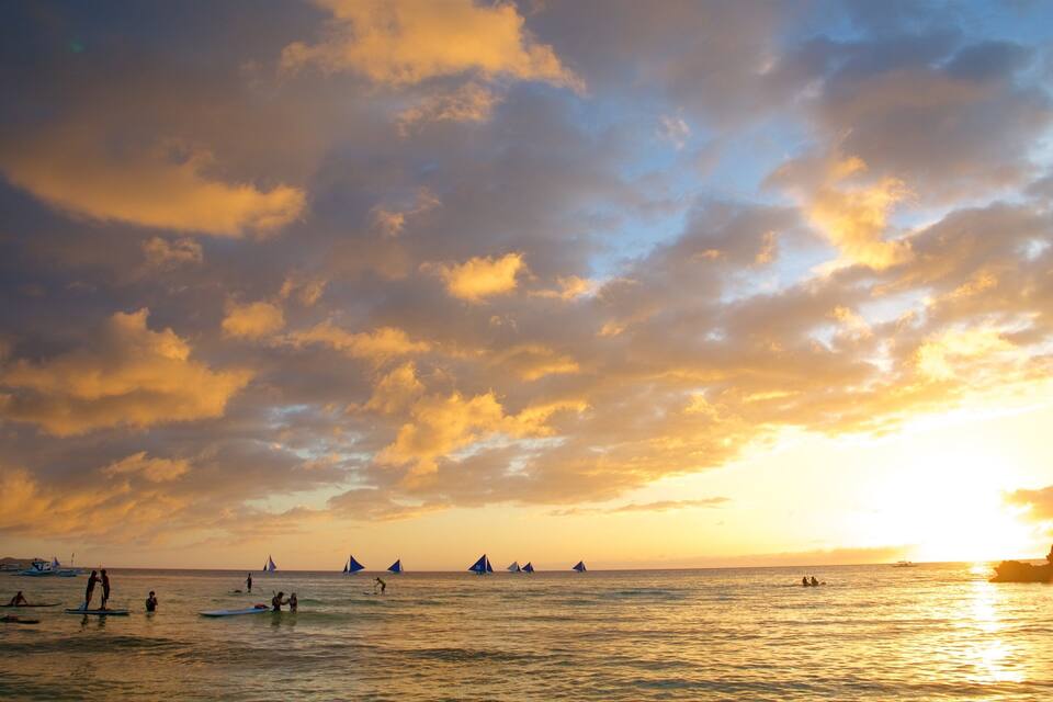 A sunset over the ocean with sailboats and people on surfboards.