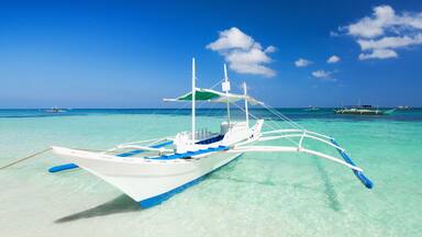 A white boat with blue accents on a turquoise sea with other boats in the background.