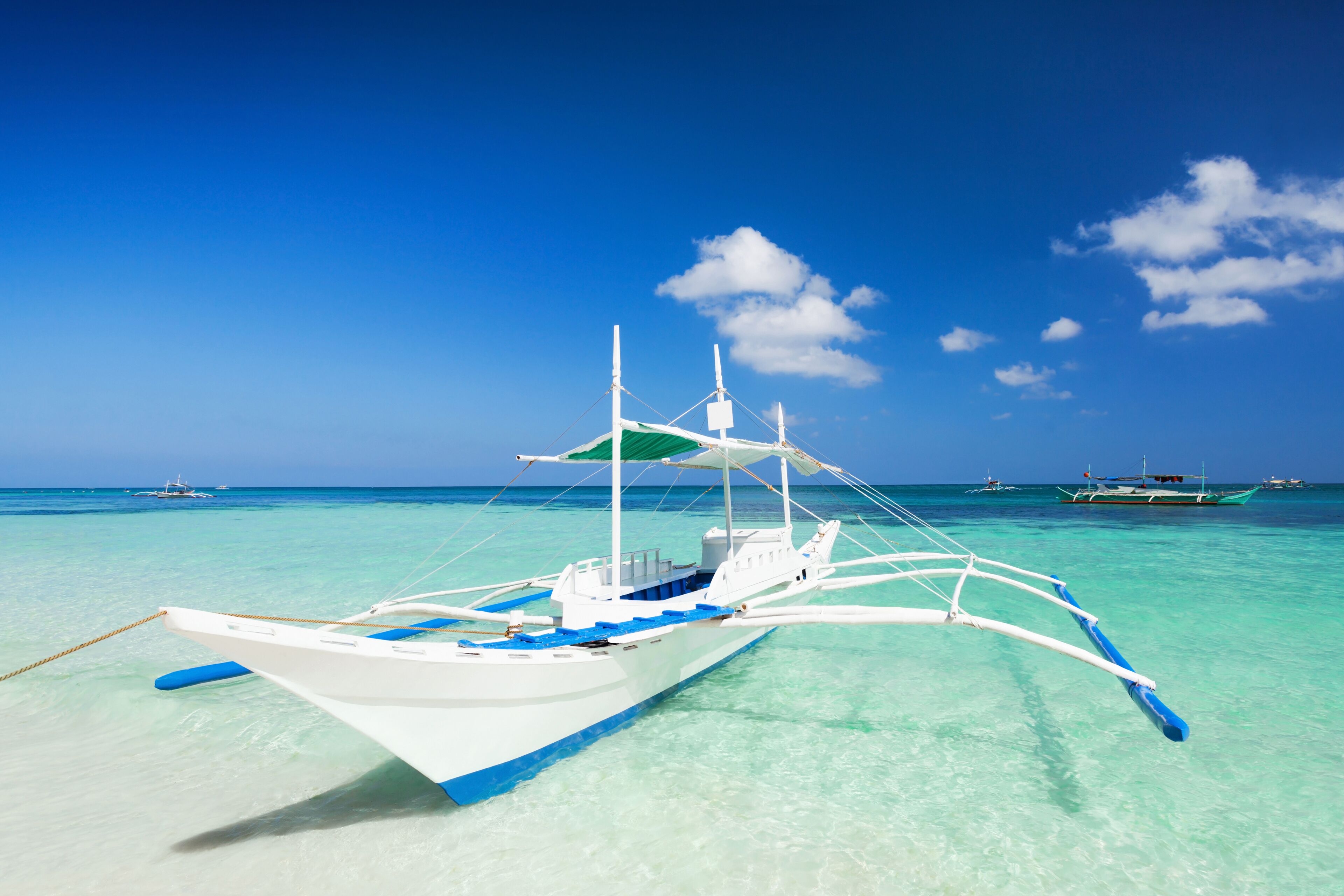 A white boat with blue accents on a turquoise sea with other boats in the background.