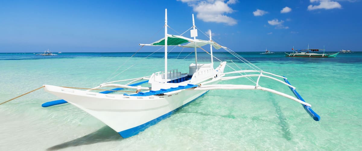 A white boat with blue accents on a turquoise sea with other boats in the background.