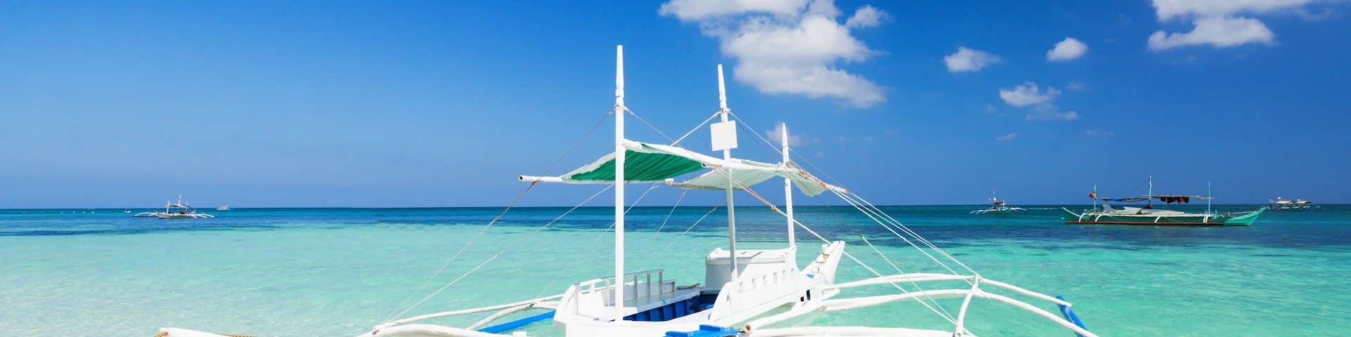 A white boat with blue accents on a turquoise sea with other boats in the background.