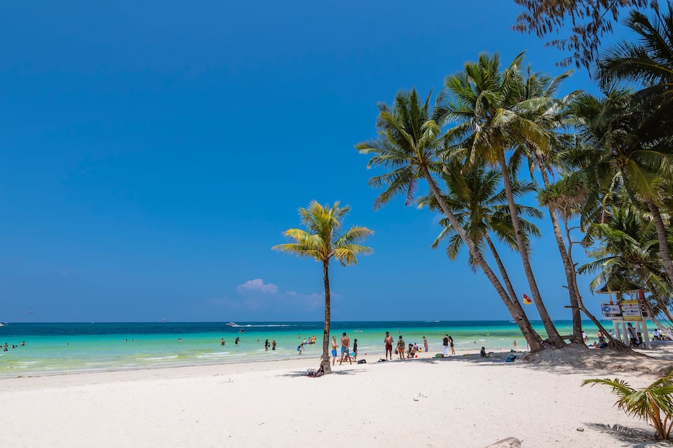 A beach with palm trees, clear turquoise water, and people enjoying the sun.