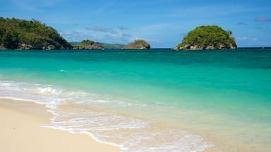 A beach with clear turquoise water, sandy shore, and two small islands with greenery.