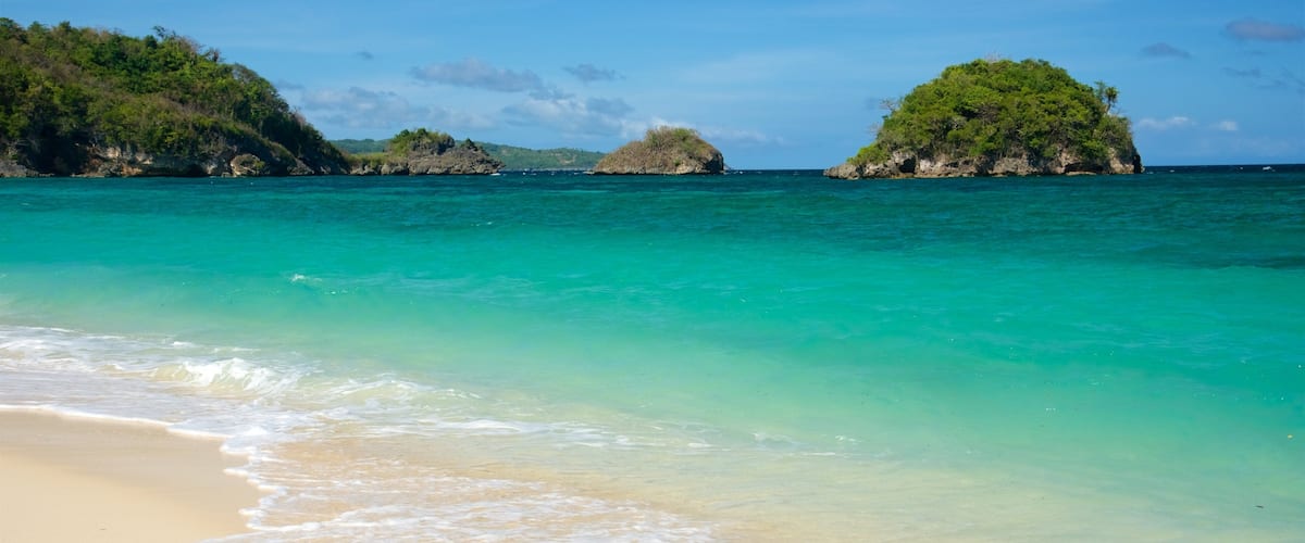 A beach with clear turquoise water, sandy shore, and two small islands with greenery.