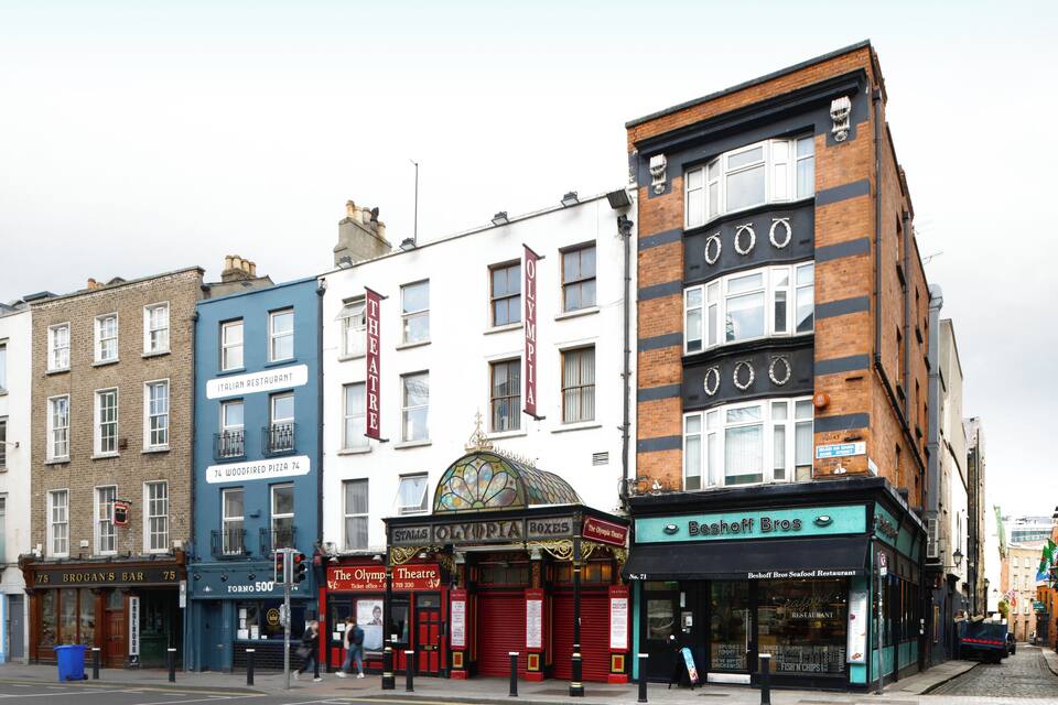 A street with various shops including a wood-fired pizza place, a theatre, and a seafood restaurant.
