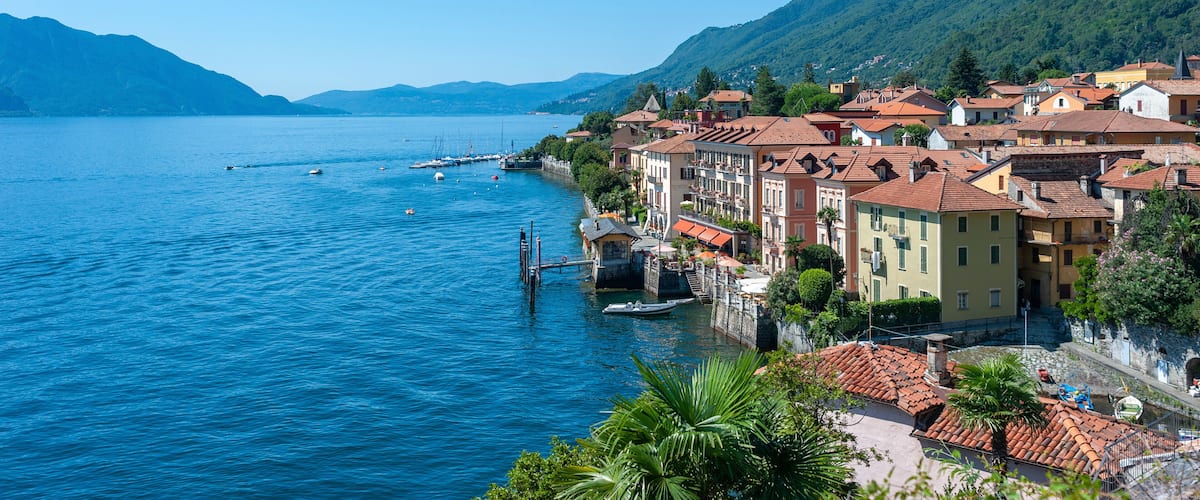 A coastal town with buildings along the waterfront, a clear blue lake, and mountains in the background.