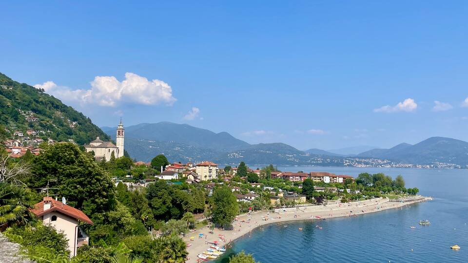 A coastal town with a prominent church tower, a beach, and mountains in the background.