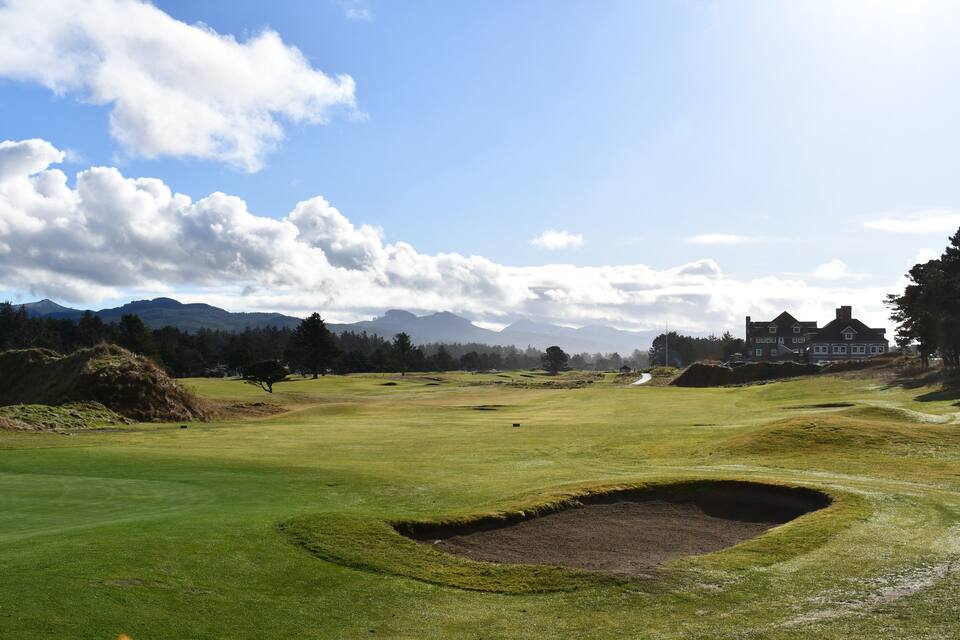 A golf course with bunkers, a clubhouse, and mountains in the background.