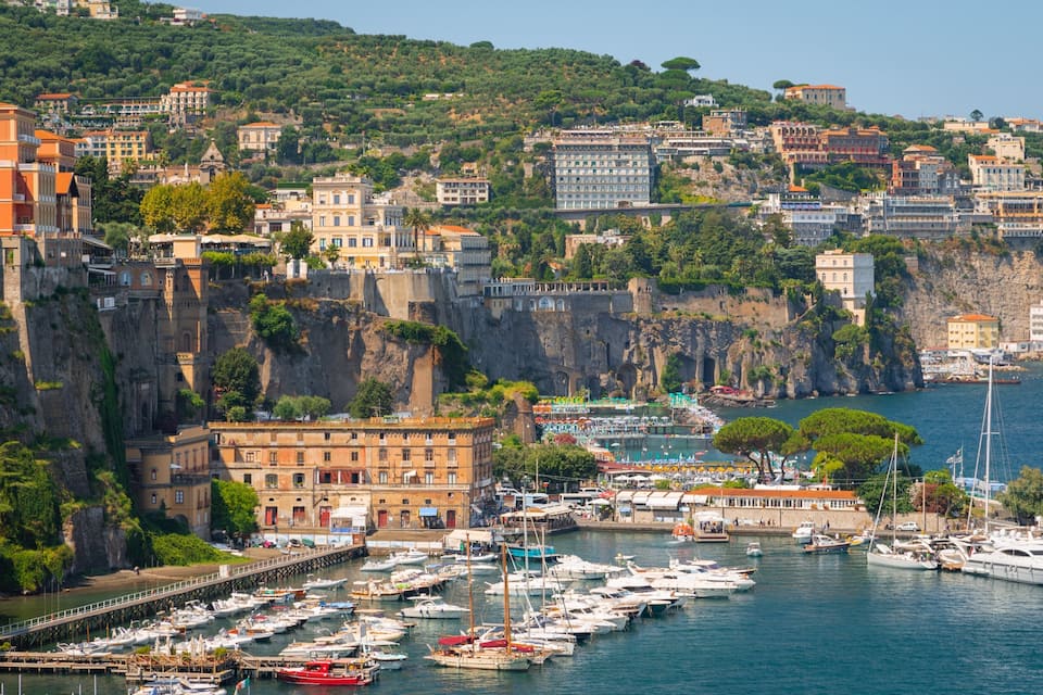 A coastal town with a marina filled with boats, historic buildings, and a steep cliffside.