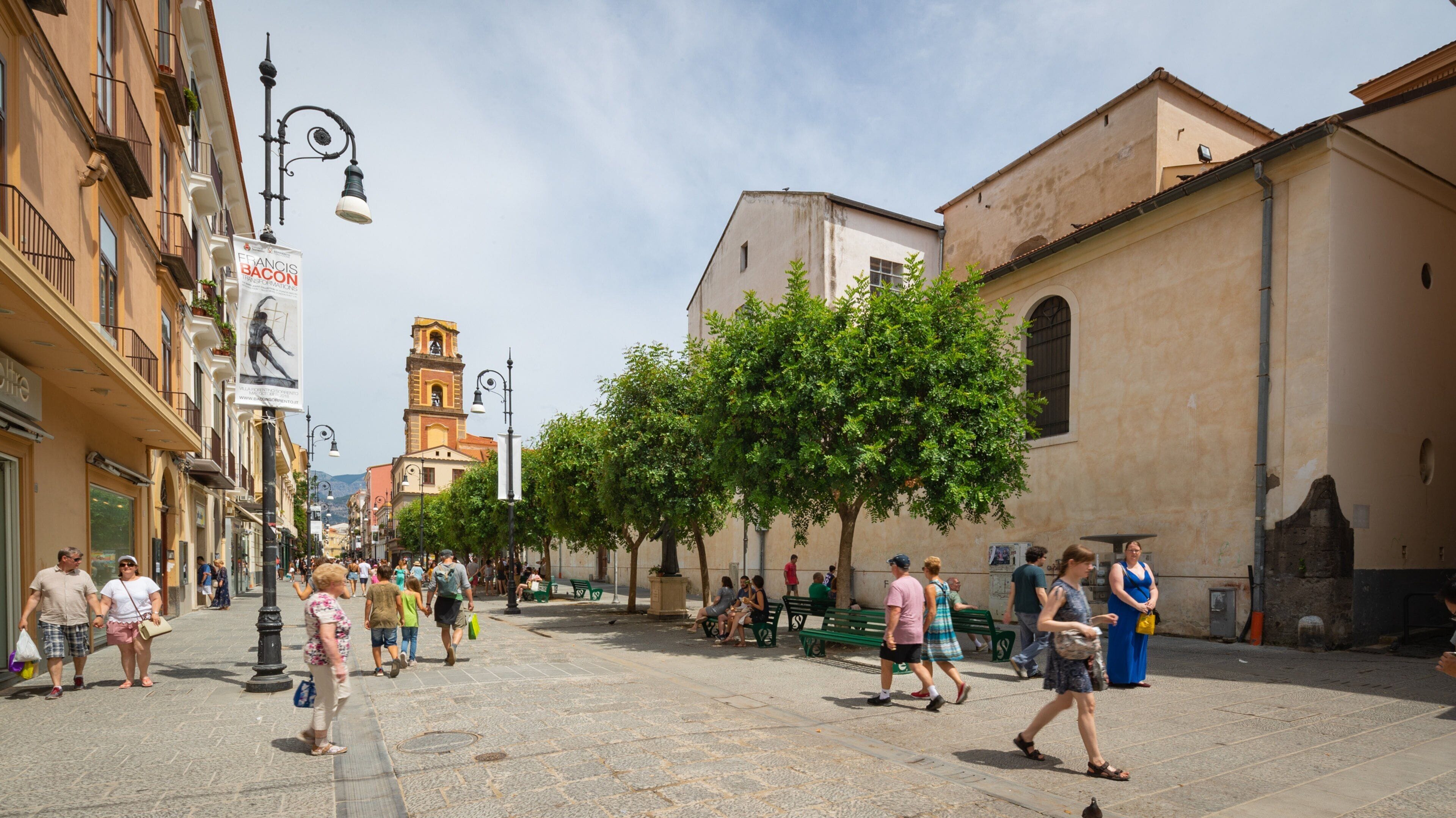 Une rue animée, fréquentée par de nombreux piétons, avec une église imposante et un clocher.
