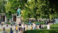 Uma estátua em um parque, rodeada por árvores e pessoas.