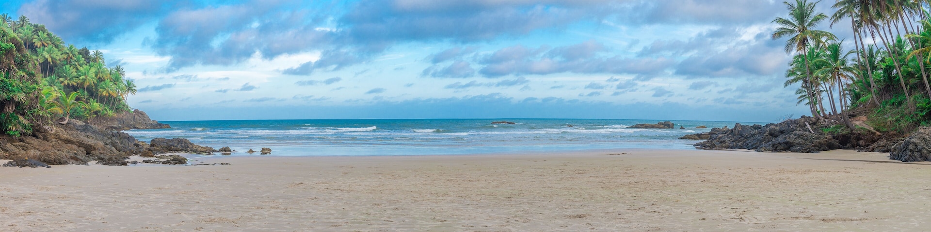 Une plage bordée d’un rivage rocheux, avec des palmiers et un ciel dégagé.
