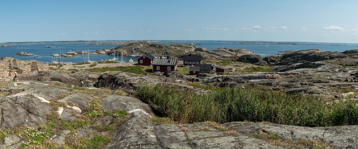 A rocky coastal landscape with a small cluster of red houses and boats in the water.