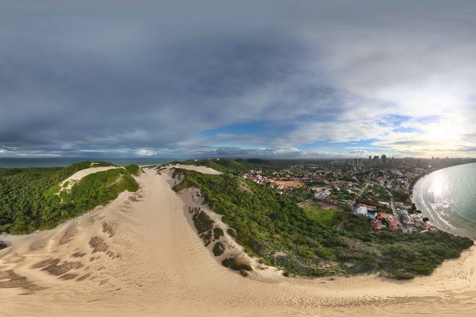 A coastal landscape with a sandy beach, green hills, and a town by the sea.