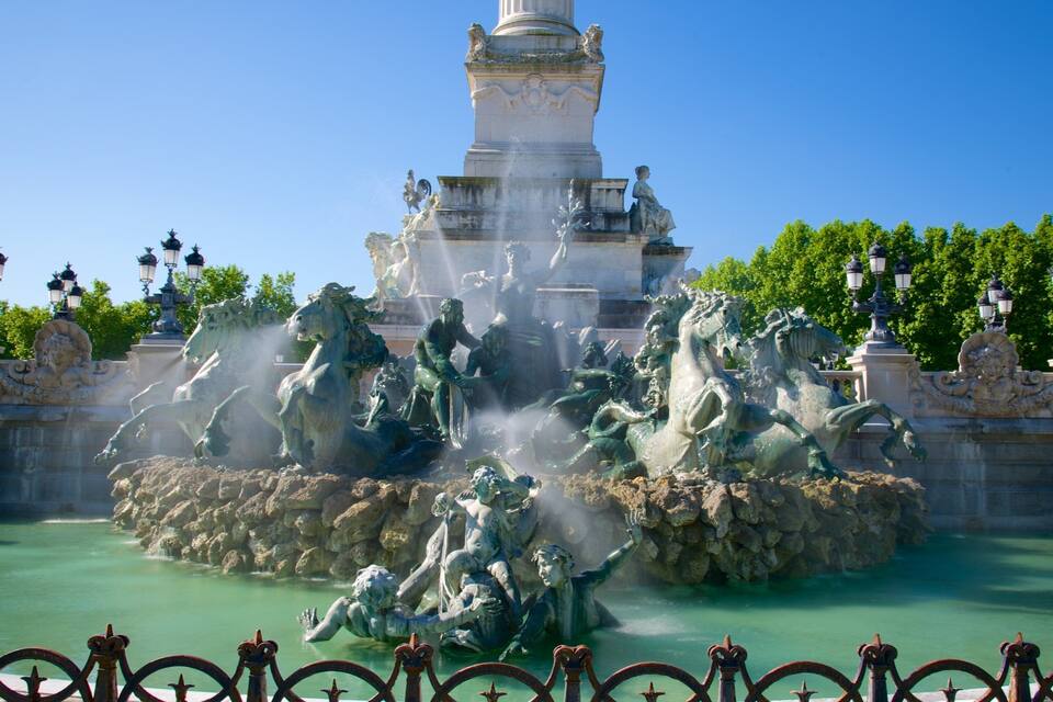 Une grande fontaine ornée de statues de chevaux et de personnes, entourée d’arbres et de lampadaires.