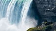 Uma grande cascata desce por um penhasco, com uma plataforma de observação e pessoas na base.