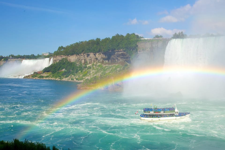 Un bateau sur une étendue d’eau, avec une cascade et un arc-en-ciel en arrière-plan.