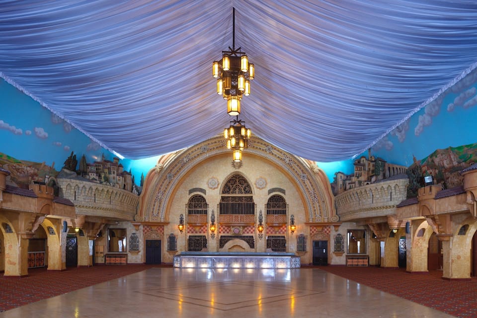 Een ruime binnenruimte met een hoge plafond, versierde bogen en een centrale kroonluchter.