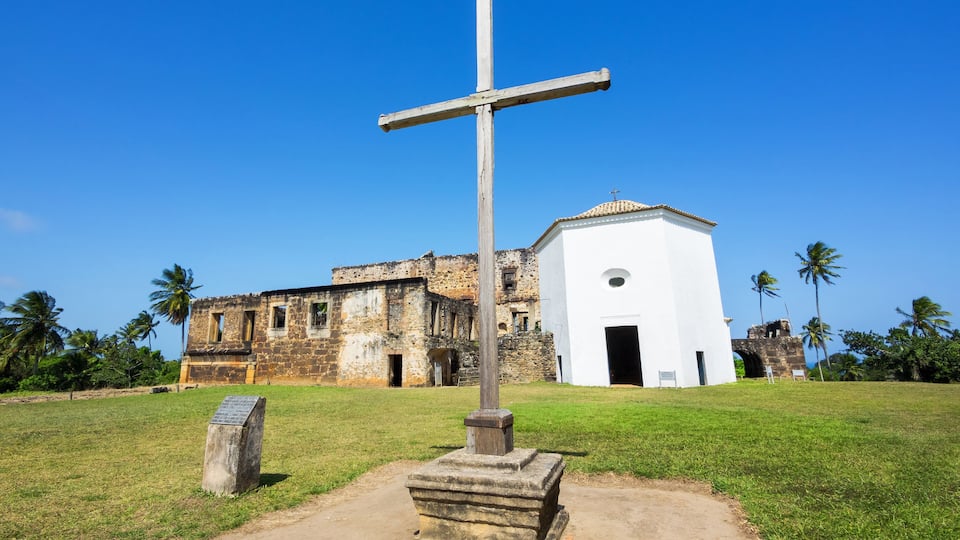 A cross, a white building, and an old stone structure.