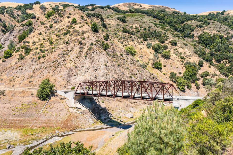 Un pont métallique enjambant une rivière dans un paysage vallonné et aride, où la végétation est rare.