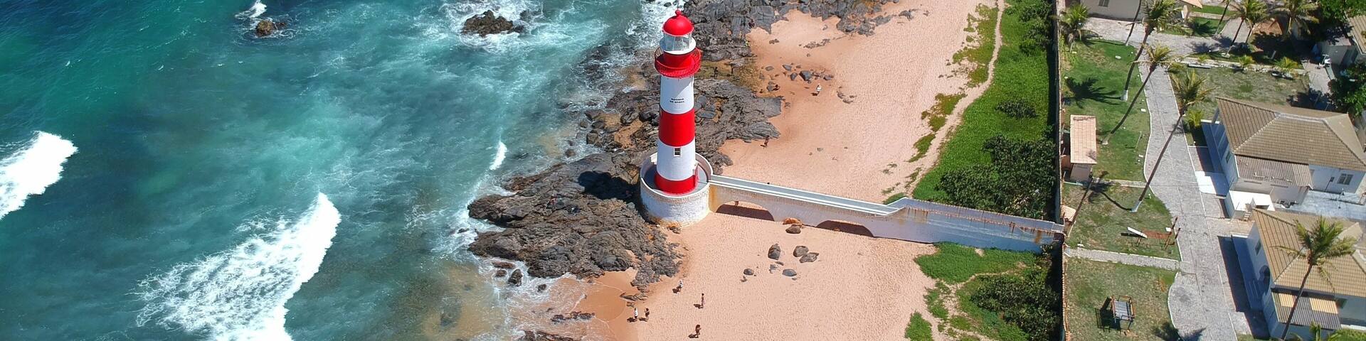A coastal landscape with a lighthouse, beach, rocky shoreline, and residential area.